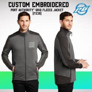 May include: A gray and black fleece jacket with a zipper closure. The jacket has a grid pattern and a contrasting black panel on the shoulders and sleeves. The text "YOUR DESIGN HERE" is embroidered on the left chest of the jacket.