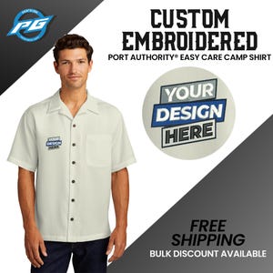 May include: A white short-sleeved camp shirt with a button-down collar. The shirt has a pocket on the left side and a small embroidered design on the left chest that says "Your Design Here". The shirt is shown on a model. The text "CUSTOM EMBROIDERED" is at the top of the image. The text "PORT AUTHORITY® EASY CARE CAMP SHIRT" is below the text "CUSTOM EMBROIDERED". The text "FREE SHIPPING" is at the bottom of the image. The text "BULK DISCOUNT AVAILABLE" is below the text "FREE SHIPPING".