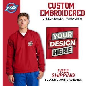 May include: Red V-neck wind shirt with long sleeves and a raglan design. The shirt has "YOUR DESIGN HERE" embroidered on the front.