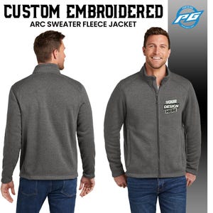 Puede incluir: Una chaqueta de forro polar gris con cierre de cremallera y un peque&ntilde;o bolsillo en el pecho izquierdo. La chaqueta tiene un cuello alto y se muestra en un modelo que lleva pantalones vaqueros azules. El texto "YOUR DESIGN HERE" est&aacute; bordado en el pecho derecho de la chaqueta.