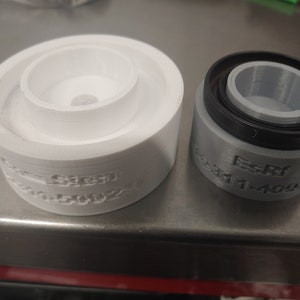 Op de afbeelding: Twee 3D-geprinte mallen, een witte en een grijze. De witte mal heeft de tekst "Sized" en "10000ZZ" aan de zijkant geprint. De grijze mal heeft de tekst "Es-Ref 03311-4092" aan de zijkant geprint.