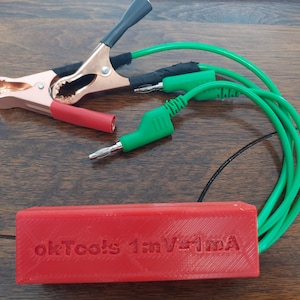 May include: A red 3D printed box with the text "okTools 1mV/1mA" on the top. The box is connected to two green wires with alligator clips on one end and banana plugs on the other.