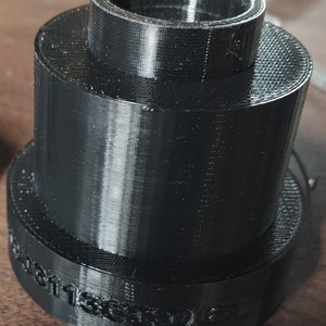 Może przedstawiać: Czarny adapter z tworzywa sztucznego, wydrukowany w 3D, z nadrukiem "screw 6" na spodzie.