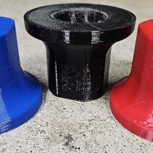 Op de afbeelding: Drie 3D-geprinte objecten in blauw, zwart en rood. Elk heeft een uitlopende basis en een cilindrische bovenkant met een gat. De blauwe en rode objecten hebben respectievelijk de letters "GR" en "UR". De objecten zijn waarschijnlijk componenten of onderdelen.