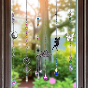May include: Decorative window suncatchers with hanging chains. Each chain features colorful beads, crystals, and charms, including a crescent moon, sun, fairy, butterfly, and lotus flower. The suncatchers are designed to catch the light and create a sparkling effect.