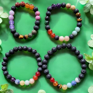 May include: Four lava rock bracelets with different colored gemstone beads. The bracelets are arranged in a square shape on a green background.
