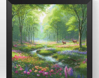Puede incluir: Un paisaje en punto de cruz enmarcado representa una serena escena forestal. La obra presenta un arroyo que serpentea a través de un prado lleno de coloridas flores silvestres. Dos ciervos se alzan a lo lejos, rodeados de exuberantes árboles verdes y un cielo brillante.