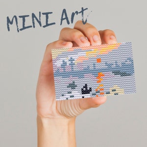 Pode incluir: Uma mão segura uma pequena peça de arte de pixel colorida com uma cena de pôr do sol. A peça de arte é feita de pequenas contas coloridas e é emoldurada por uma borda branca. O texto "MINI Art" está escrito acima da mão.