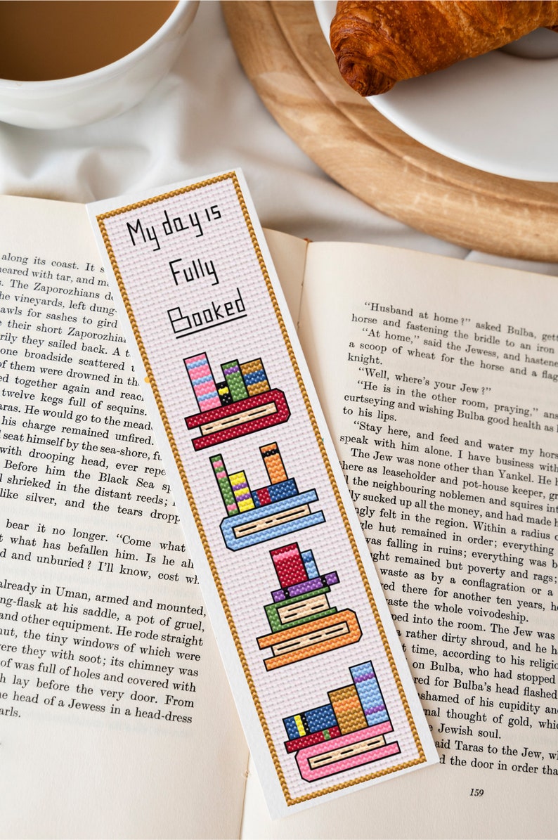 May include: A pink and white bookmark with a gold border. The bookmark features the text "My day is Fully Booked" and three stacks of colourful books.