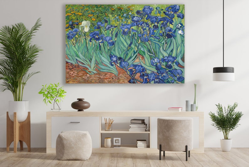 May include: A painting of a field of blue irises with green leaves. The painting is in a modern living room setting with a white wall, a wooden table, and a potted plant.