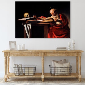 May include: A painting of a man with a long white beard sitting at a table and writing in a book. He is wearing a red robe and a halo. A skull is on the table next to him.