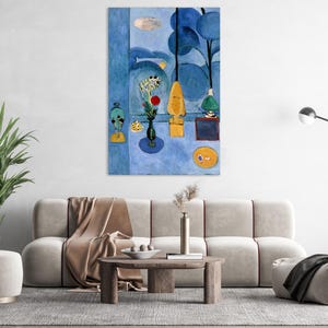 May include: A large, framed abstract painting with a blue and yellow color palette. The artwork features stylized shapes, including trees, vases, and a sun-like circle. The painting is displayed above a beige sofa in a living room setting.