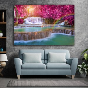 May include: A vibrant landscape painting featuring a cascading waterfall surrounded by lush greenery and pink flowering trees. The water flows over rocks and creates a tranquil scene.