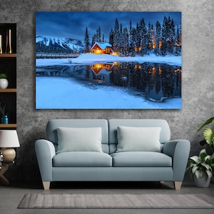 May include: A wooden cabin with lit windows sits on a snow-covered lakeshore, surrounded by a forest of evergreen trees. The cabin is reflected in the still, blue water of the lake.