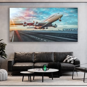 May include: A white airplane taking off from a runway at an airport. The airplane is in the foreground of the image, and the runway is in the background. The sky is blue and there are clouds in the sky. The sun is setting in the background.
