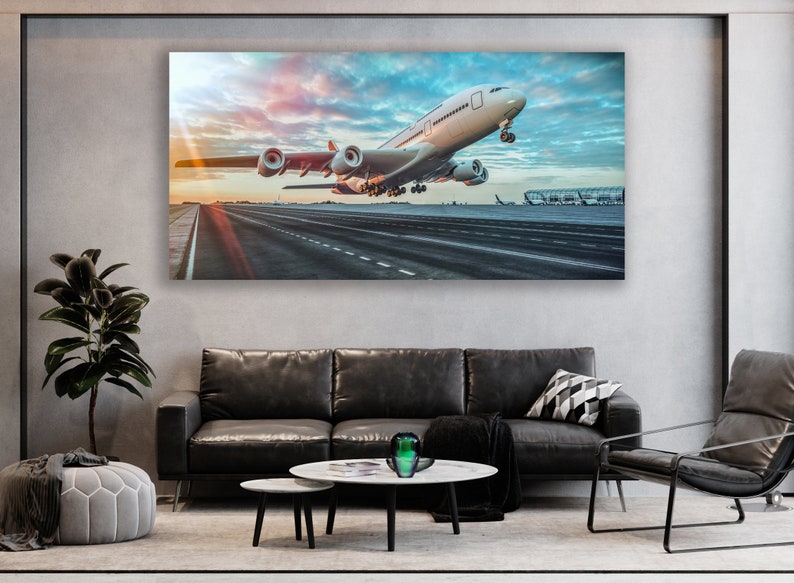 May include: A white airplane taking off from a runway at an airport. The airplane is in the foreground of the image, and the runway is in the background. The sky is blue and there are clouds in the sky. The sun is setting in the background.