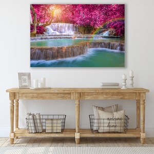May include: A canvas print of a waterfall cascading through a lush forest with vibrant pink trees. The water is clear and turquoise, and the trees are in full bloom.