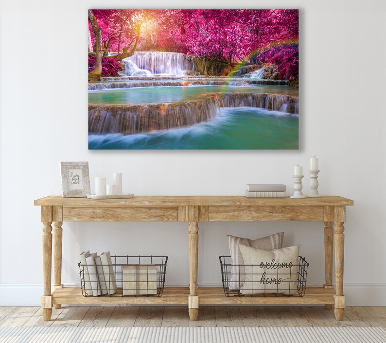 May include: A canvas print of a waterfall cascading through a lush forest with vibrant pink trees. The water is clear and turquoise, and the trees are in full bloom.