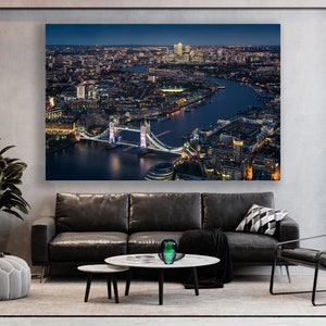 May include: An aerial view of London at night, showing the Tower Bridge lit up with lights. The River Thames flows through the city, with buildings and streets visible in the distance.