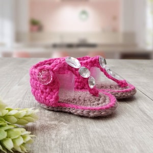 May include: A pair of pink crocheted baby sandals with clear rhinestone embellishments.
