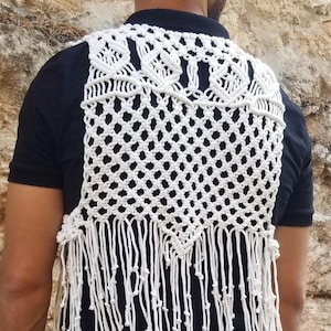 Op de afbeelding: Wit gebreid vest met een geometrisch patroon en franjes. Het vest is gemaakt van katoenen koord en heeft een delicate, luchtige uitstraling.