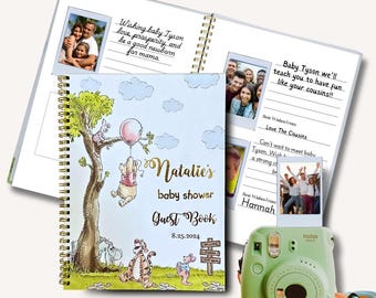 May include: A spiral-bound baby shower guest book with a Winnie the Pooh theme. The cover features illustrations of Pooh, Piglet, and Tigger. The book includes space for photos and well wishes. A green Instax camera is also in the image.
