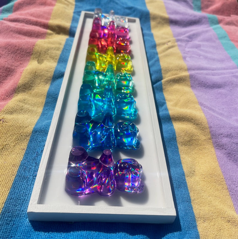 May include: A white frame with a rainbow of gummy bears, each one is a different color and has a shiny, iridescent finish.