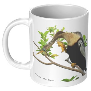 May include: White ceramic mug with a colorful image of an Anhinga bird perched on a branch. The bird has a long neck and a black and white patterned body. The text "Anhinga - Matt Yubas" is printed on the bottom of the mug.