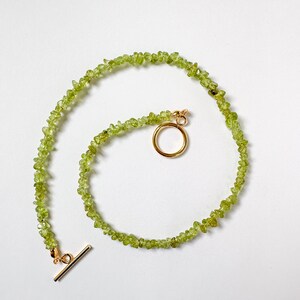 May include: A green gemstone necklace with a gold clasp and a toggle closure. The necklace is made of small, irregularly shaped stones.