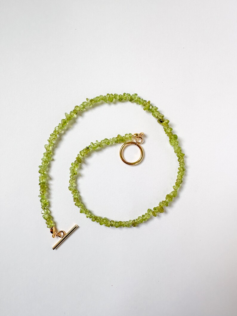 May include: A green gemstone necklace with a gold clasp and a toggle closure. The necklace is made of small, irregularly shaped stones.