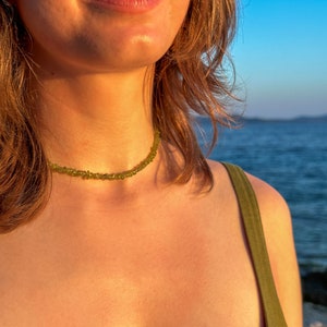 May include: A woman wearing a green tank top with a delicate green gemstone necklace. The necklace is made of small, irregular shaped stones.