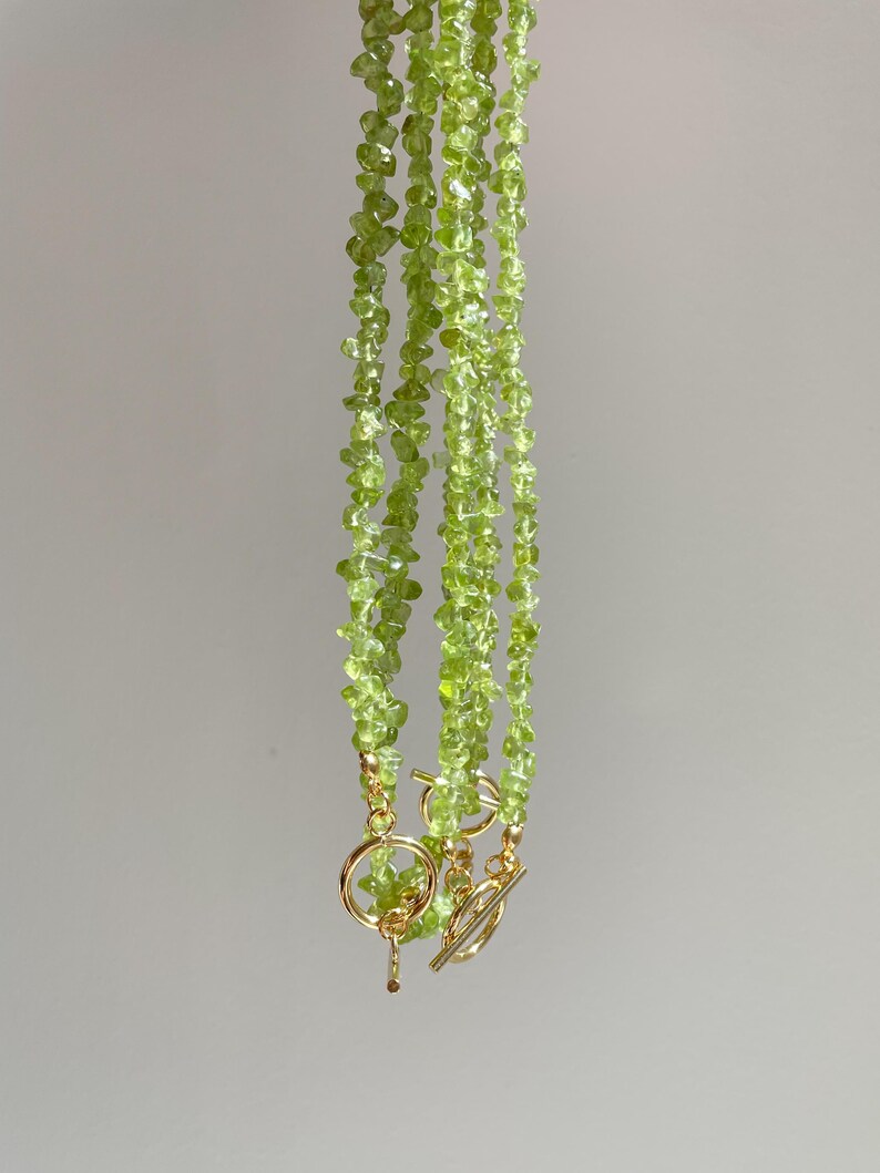 May include: A set of three green gemstone necklaces with gold clasps. The necklaces are made of small, irregular shaped green stones.