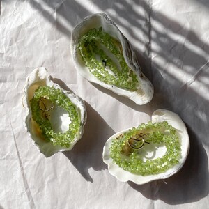 May include: Three white seashells with green gemstone necklaces inside. The necklaces are made of small, irregular shaped green stones and have gold clasps.