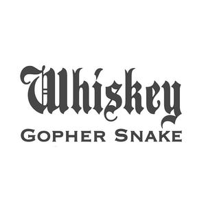 May include: The image shows the words "Whiskey Gopher Snake" in a dark grey, gothic font against a white background. "Whiskey" is in a larger, more elaborate font than "Gopher Snake".