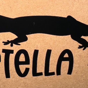 May include: Black silhouette of a gecko with the name "STELLA" written underneath in a bold, black font.