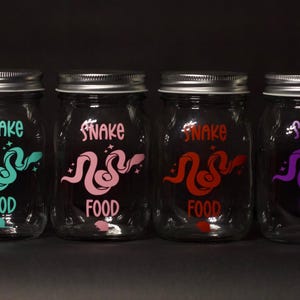 May include: Four glass jars with silver lids, each labeled "Snake Food" with a different colored snake design: teal, pink, red, and purple.
