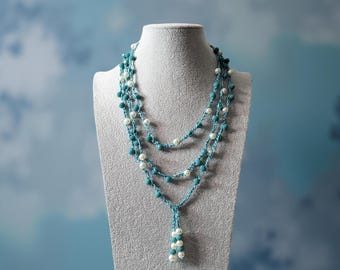 May include: A three-strand necklace displayed on a mannequin. The necklace features turquoise and white beads strung on a delicate chain. The necklace has a cascading design, with a cluster of white beads at the bottom.