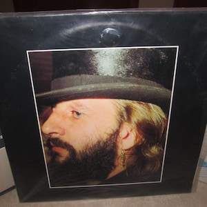 May include: A black and white photograph of a man with a beard wearing a black top hat. The man is looking to the left of the photograph.