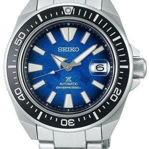 Könnte beinhalten: Eine silberne Seiko-Uhr aus Edelstahl mit blauem Zifferblatt und schwarzer Lünette. Die Uhr hat ein Datumsfenster bei 3 Uhr und eine weiße Aufschrift 'Automatic Diver's 200m'.