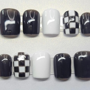 May include: A set of ten artificial nails in various designs. The nails feature solid black, solid white, and black and white checkered patterns. The nails are rectangular and have a glossy finish.