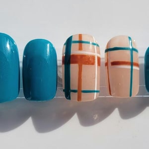 May include: A set of press-on nails in various designs. Two nails are solid teal, while two feature a beige base with teal and orange plaid patterns. The last nail is solid teal. All nails have a glossy finish.