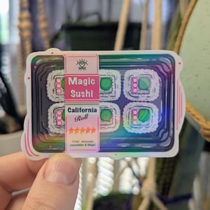May include: A sticker featuring a colorful illustration of sushi rolls in a takeout container. The sticker reads "Magic Sushi" and "California Roll" with a list of ingredients. The sticker has a holographic effect.