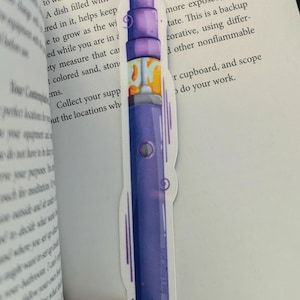 May include: A purple and white vape pen bookmark with a stylised eye design. The bookmark is a fun and quirky way to mark your place in a book.
