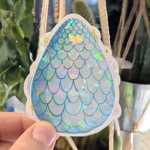 May include: A blue iridescent sticker of a dragon egg with gold glitter accents.