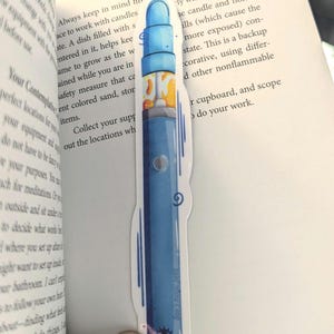 Peut inclure: Un marque-page en forme de stylo vape bleu et jaune sur fond blanc. Le marque-page est un gros plan du stylo vape et ne montre pas le marque-page entier.