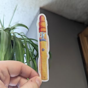 Peut inclure: Un autocollant jaune et orange représentant un stylo vape de dessin animé avec une finition scintillante.