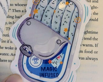 May include: A sticker featuring a whimsical illustration of a sardine can. The can is open, revealing stylized fish with star and swirl accents. The label reads "MAGIC INFUSED" in a blue and white design.