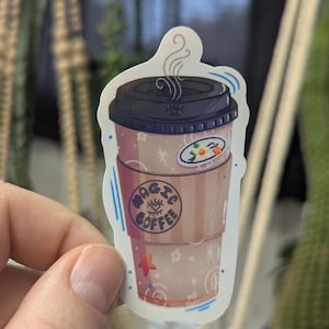 May include: A sticker depicting a coffee cup with a black lid and a brown sleeve. The sleeve has the words "MAGIC COFFEE" and an eye symbol. The cup is decorated with stars and a small sticker that says "7:23". Steam rises from the top of the cup.