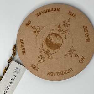 May include: A circular wooden divination board with a compass design and the words "Yes", "No", "Maybe", and "Rephrase" around the edge. The board is brown and has a light wood grain.