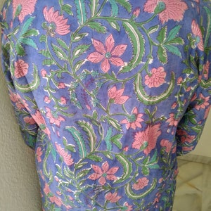 May include: A blue cotton tunic with a floral print in shades of pink and green. The print features a repeating pattern of flowers and leaves.